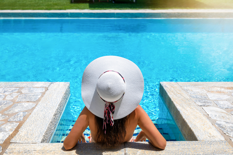 A woman in bikini and with white hat is relaxing in a swimming pool