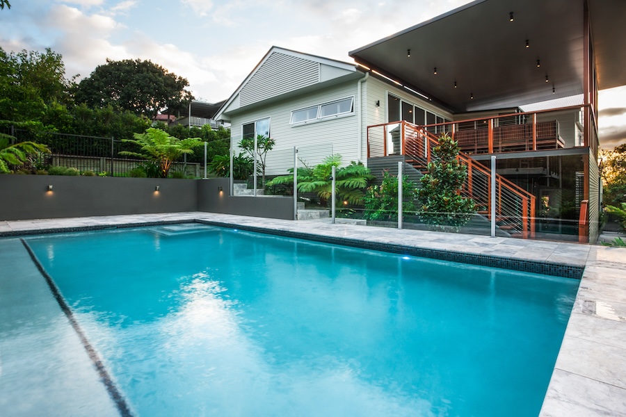 Modern pool close up with light blue water beside a mansion with a beautiful garden.