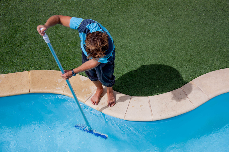 Man on edge of pool cleaning the clear salt water