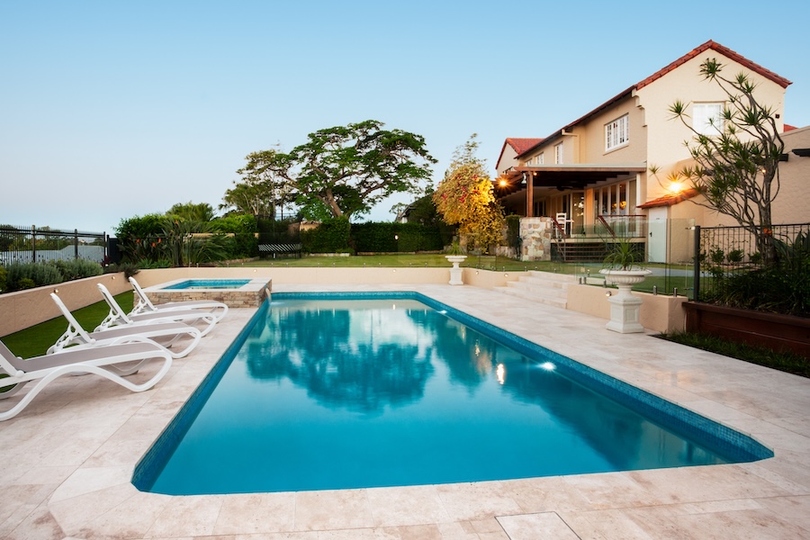 Light blue water swimming pool of a luxurious mansion with chairs around it.