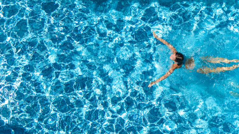 Aerial drone view of active girl in swimming pool from above, yong woman swims in blue water, tropical vacation, holiday on resort concept