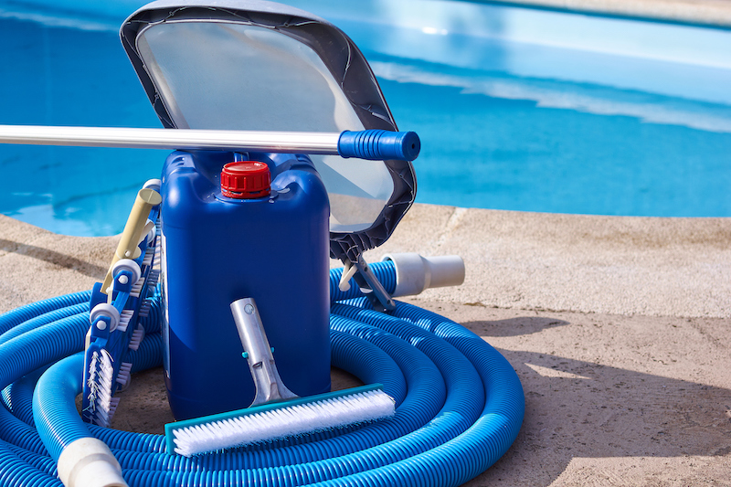 Pool equipment with cleaning chemicals and tools on the pool curb. Swimming pool at the bottom. Horizontal composition. Front view.