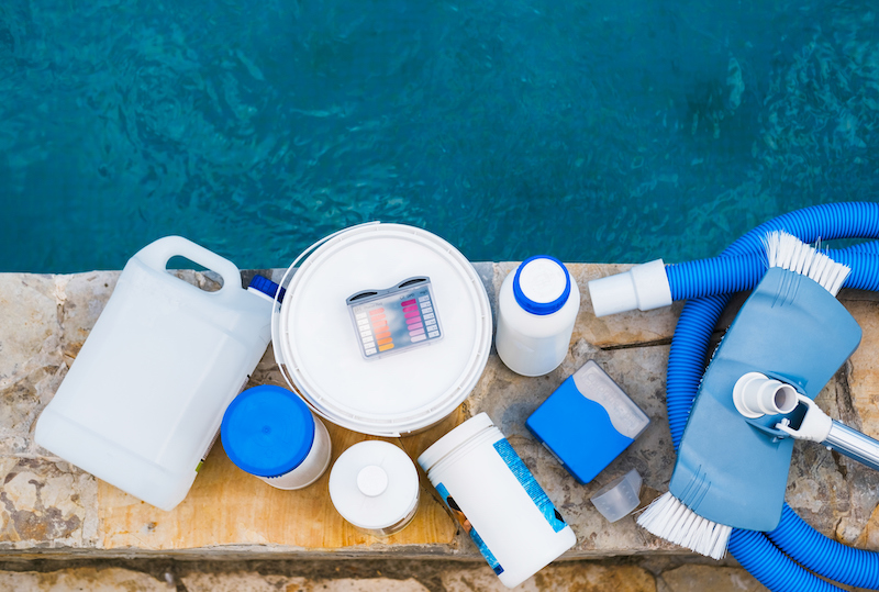 High angle view of equipment for testing the quality of pool water, vacuum cleaner and chemical cleaning products at the edge of swimming pool.