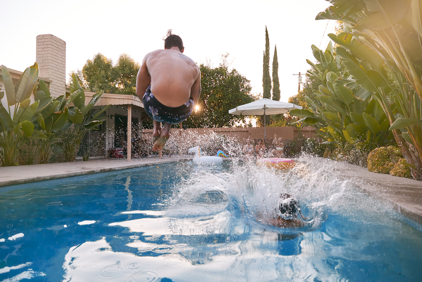 Women Outdoors Relaxing At Summer Pool Party Watching Men Dive Into Water