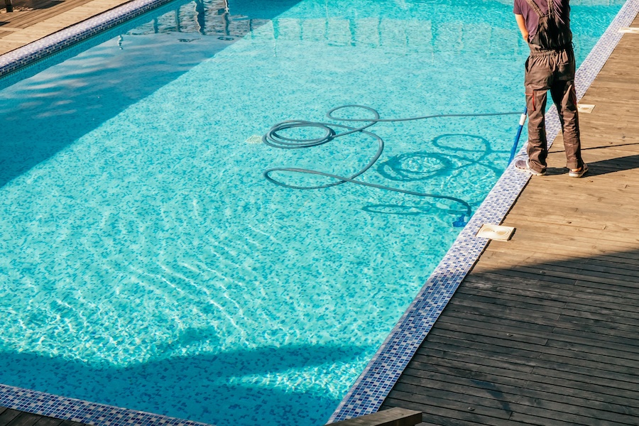 Man cleaning the swimming pool with vacuum equipment.