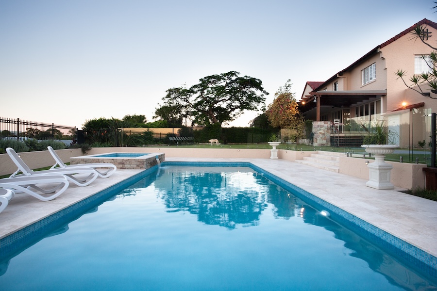 Modern swimming pool water close up beside chairs on the tiled floor in front of the luxury house