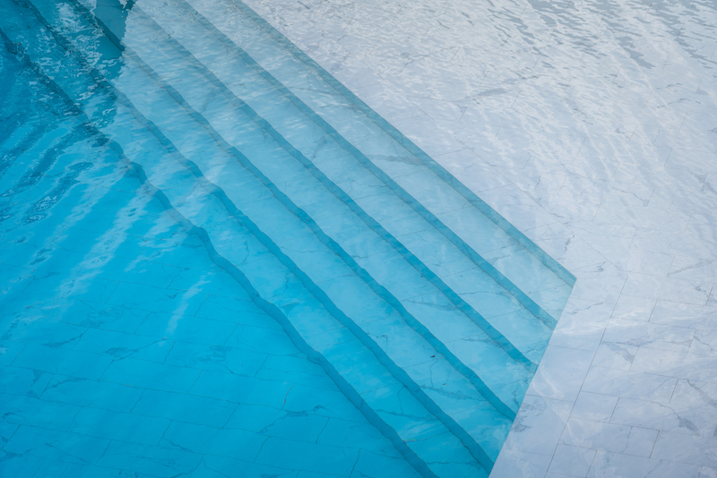 Beautiful designed swimming pool with transparent blue water and white marble luxury floor. Sport recreation and background photo.