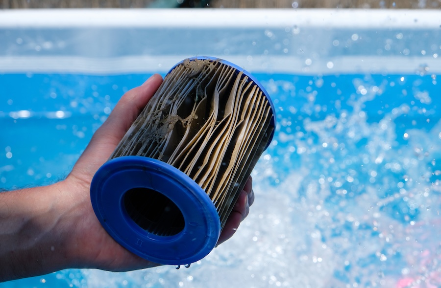 Dirty Replacement Pool Filter Cartridge in a man's hand on water splash background.