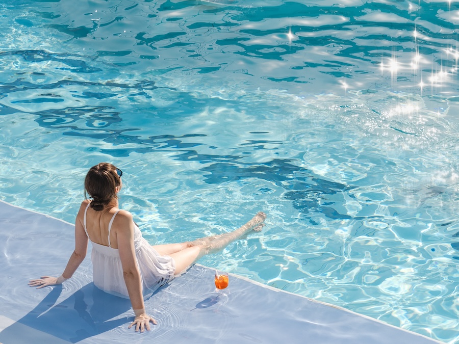 Cute woman with a glass of drink sits near the swimming pool