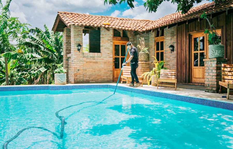 Maintenance and cleaning of home swimming pool with vacuum suction hose. Male worker cleaning a beautiful swimming pool with vacuum suction hose