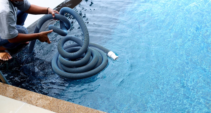 Worker clean private swimming pool with vacuum blue tube cleaner