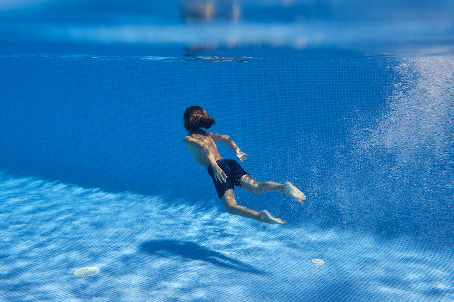 From behind of anonymous kid surrounded with air bubbles diving into tiled swimming pool