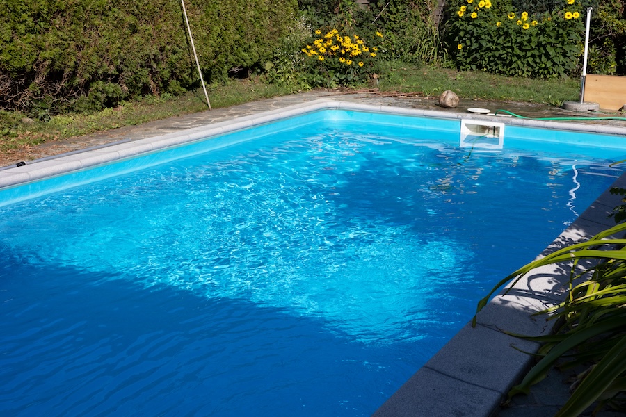 Clear water in a blue pool in the garden. Surrounded by stone paths and plants.