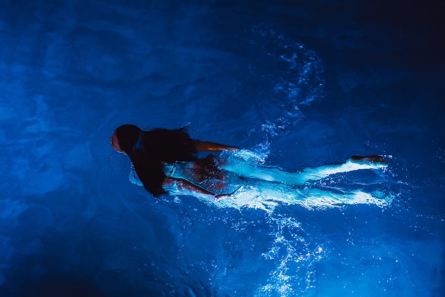 Calm beautiful young woman relaxing in a swimming pool at night, view from above. 