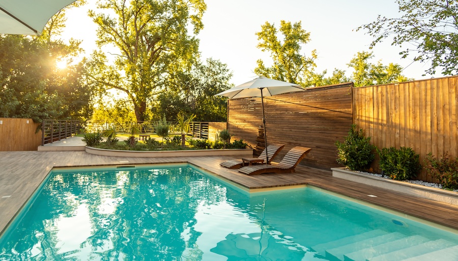 Swimming pool in modern private villa with lounge chairs, palm trees and umbrella at sunset