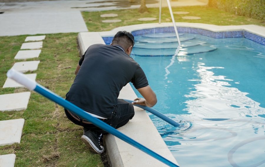 Maintenance person cleaning swimming pool with suction hose.