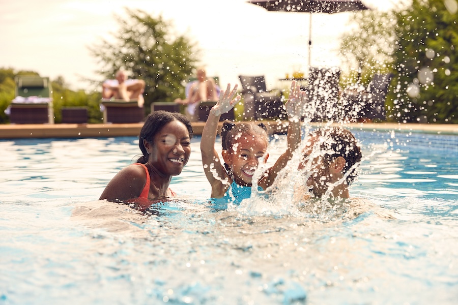 Smiling Mixed Race Family On Summer Holiday Having Fun Splashing In Outdoor Swimming Pool