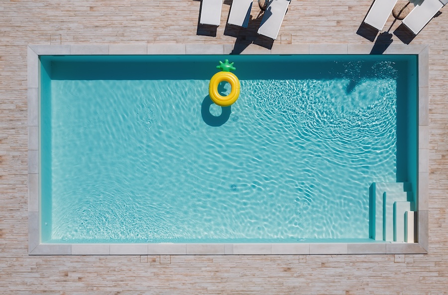 Empty rectangular blue swimming pool with sunbeds and umbrellas and big inflatable Yellow Pineapple floating tube