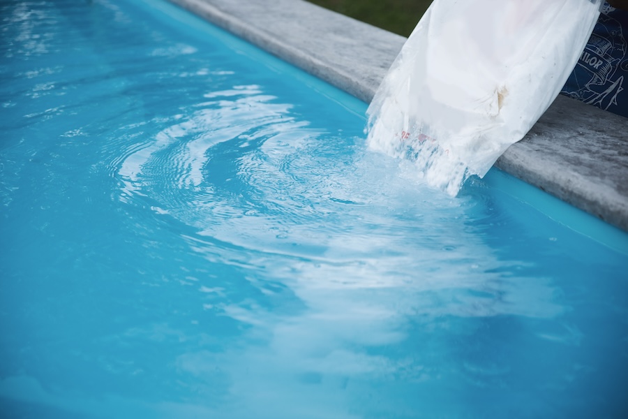 Service worker pouring salt in swimming pool water