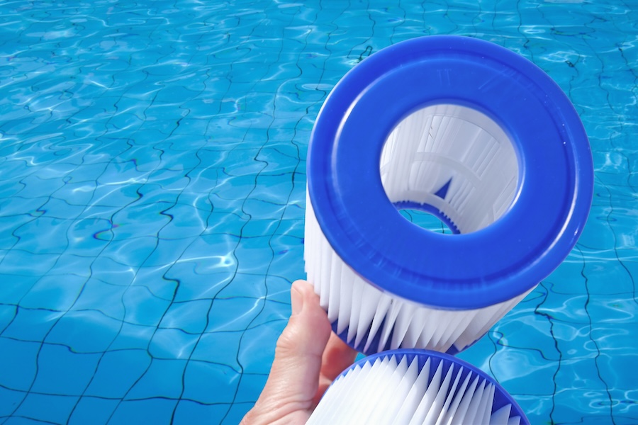 Reusable pool cartridge filters are in a human hand on pool water backdrop. 