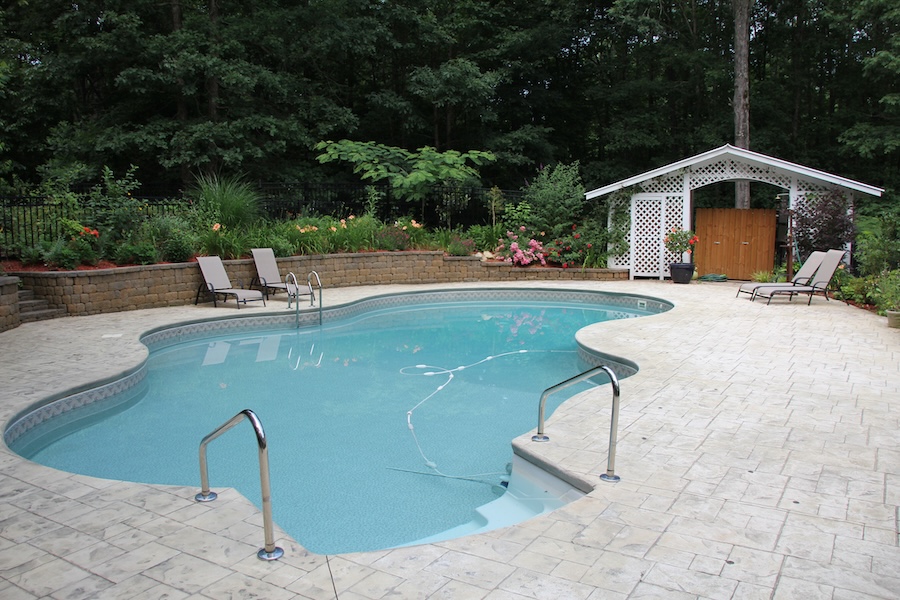 a pool surrounded by white tile and greenery