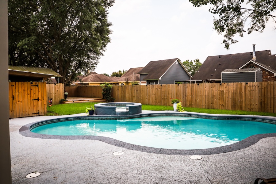 A large free form gray grey accent swimming pool with turquoise blue swim water in a fenced in backyard in a suburb neighborhood.