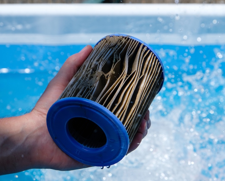 Dirty Replacement Pool Filter Cartridge in a man's hand on water splash background. Pool water quality concept.