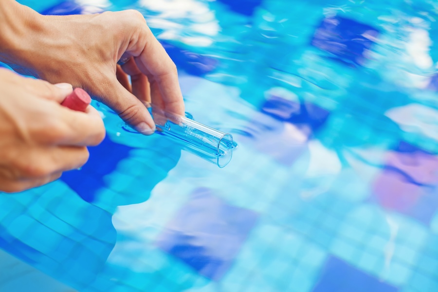 Taking a water sample from a swimming pool in a flask.