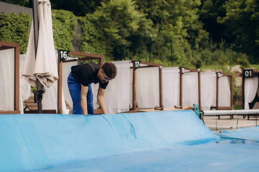 Pool maintenance worker covering an outdoor luxury resort pool with a blue tarp, ensuring protection and cleanliness for the summer season