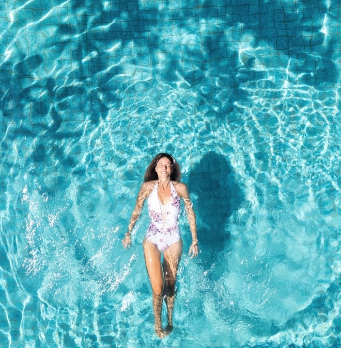 Young woman with swimsuit floating and relaxing in a turquoise swimming pool water in summer vacation