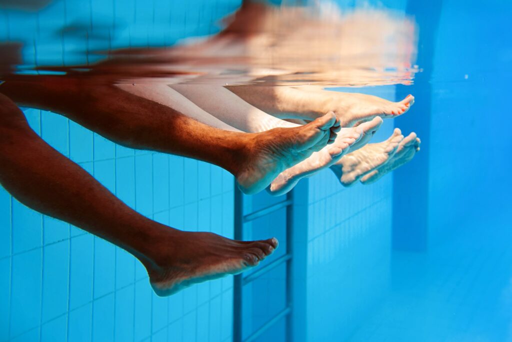 Legs of African American man with caucasian friends in swimming pool underwater. Summer. Vacation, international and sport concept.