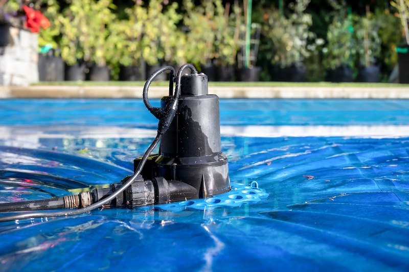 automatic-pool-cover-pump-on-top-of-blue-wet-cover-in-front-of-defocused-garden-foliage-2