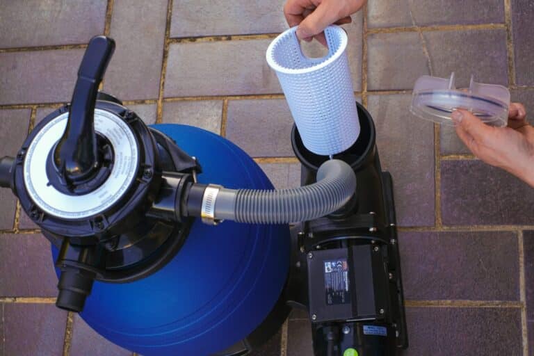 Blue swimming pool water filter in the hands of a man in a plaid shirt on terrace near the house.man moves the hoses to the filter in the pool close-up.