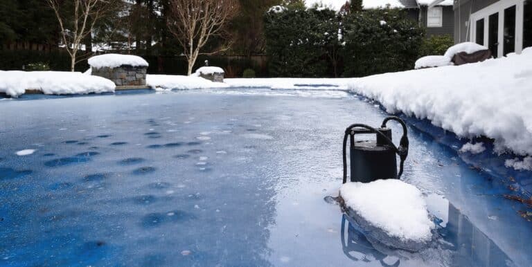 Automatic pool pump in ice and slush after snow storm. Inground backyard pool with black pool pump submerged in deep frozen water.