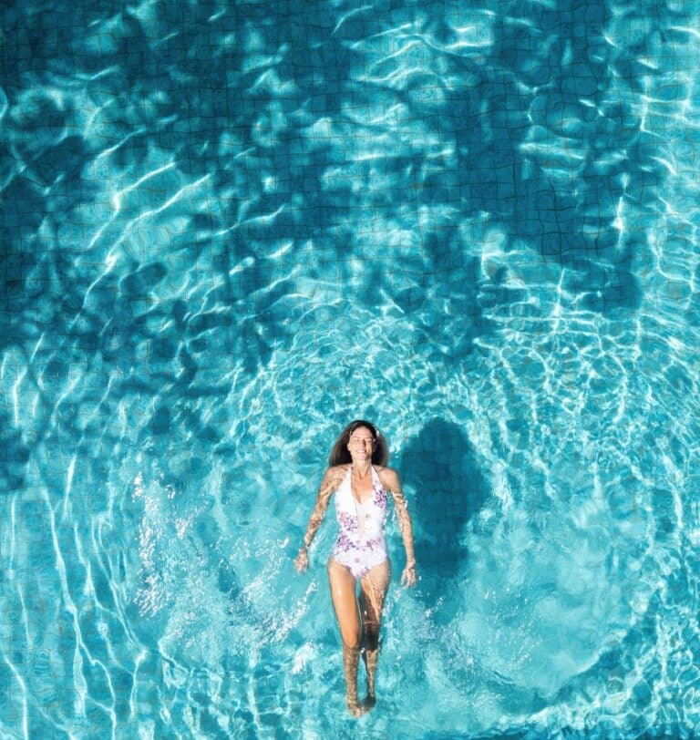 Young woman with swimsuit floating and relaxing in a turquoise swimming pool water in summer vacation