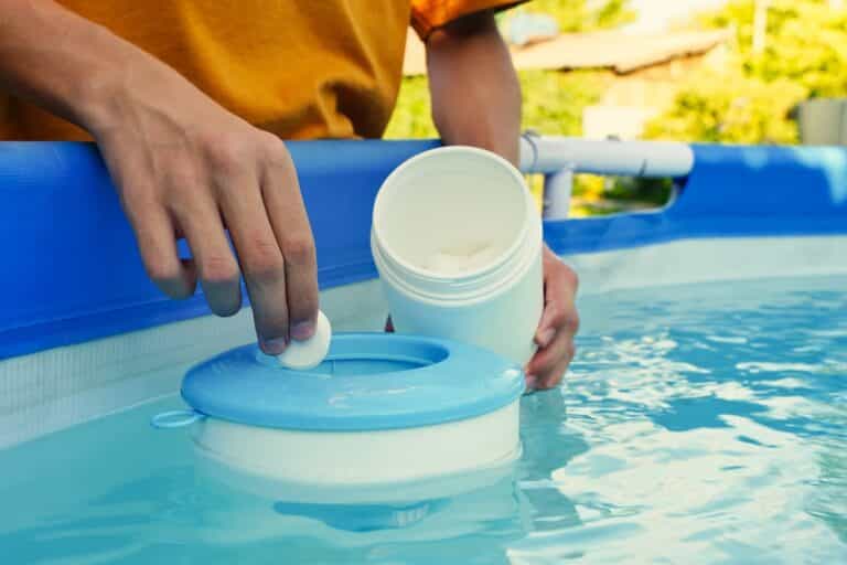 Hand holding white tablets over swimming pool skimmer.