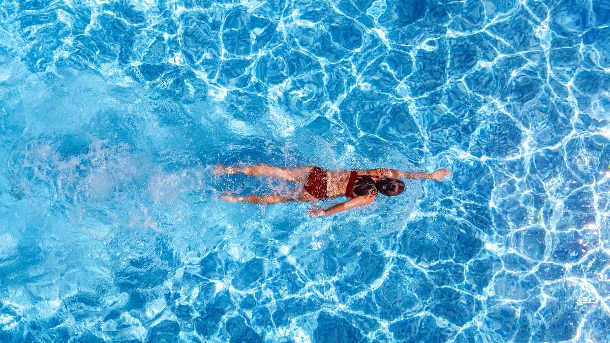 Active girl in swimming pool aerial drone view from above, young woman swims in blue water pool
