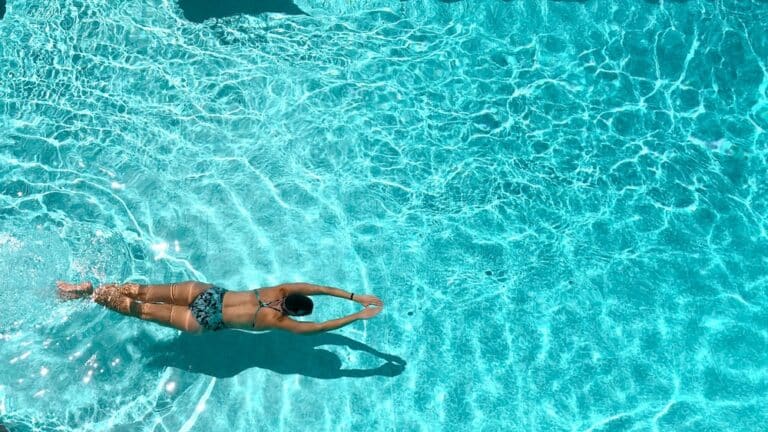 Woman in bathing suit swimming in blue pool water in summer