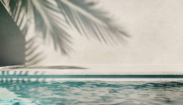 Poolside summer background with plaster wall, pool water and palm shadow.