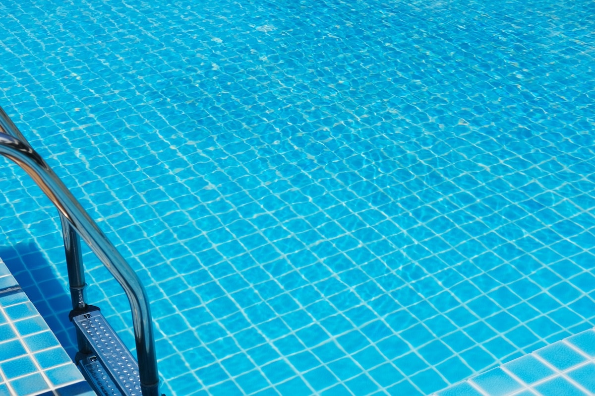 Clear blue water fills a swimming pool with a tiled surface, complemented by a stainless steel ladder