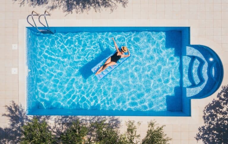 Young woman in a swimsuit and straw hat floating on blue swimming pool.